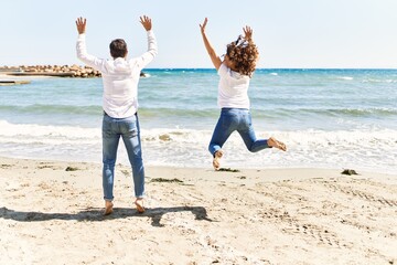 Middle age hispanic couple on back view jumping at the beach.