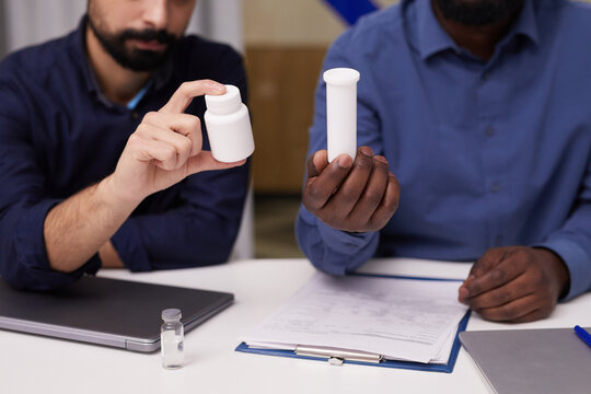 Two young intercultural male pharmacologists presenting new improved supplements or vitamins developed in chemical laboratories - Powered by Adobe