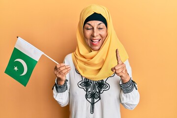 Middle age hispanic woman wearing hijab holding pakistan flag smiling with an idea or question pointing finger with happy face, number one