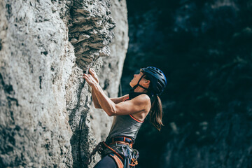 Woman climbing a rock with extreme effort in a vertical rock wall - obrazy, fototapety, plakaty