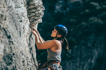 Woman climbing a rock with extreme effort in a vertical rock wall - obrazy, fototapety, plakaty