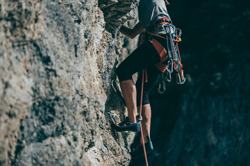 Detail of climb gear and equipment attached to a woman climbing harness while she climbs a route