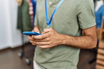 Handsome hispanic man working as shop assistance using smartphone at retail shop