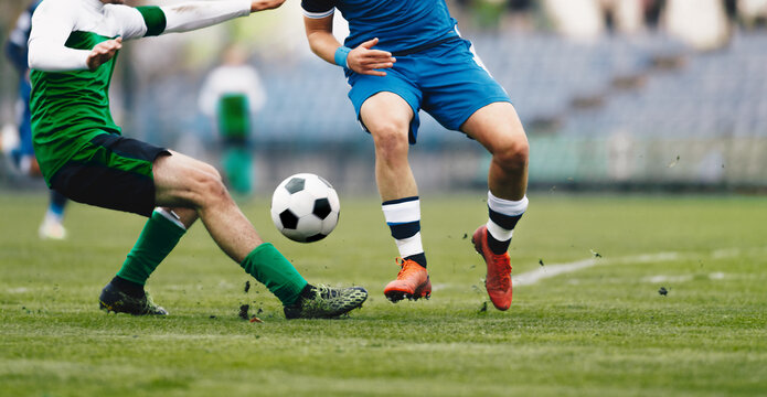 Two Football Men Running Ball In A Duel. Adult Soccer Players In Competition Game. Athletes Kicking Soccer Ball On Grass Pitch