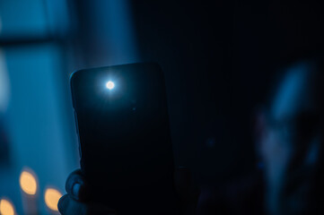 Male hand holds a smartphone with a burning flashlight with lighting window on the background. - obrazy, fototapety, plakaty