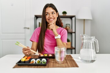 Young brunette woman eating sushi using chopsticks with hand on chin thinking about question, pensive expression. smiling and thoughtful face. doubt concept.