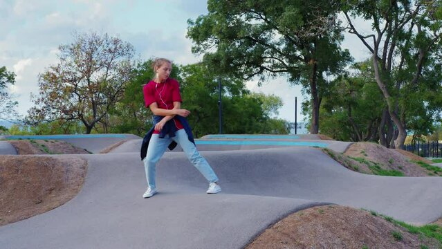 Sportive girl in earphones performing modern dances, hip hop, shuffle or contemporary outside. Young lady moving rhythmically, practicing before staging. Teen in jeans dancing at street. Youth culture