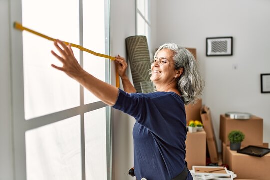 Middle age grey-haired woman smiling happy repairing window at new home.