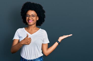 Young african american woman wearing casual white t shirt showing palm hand and doing ok gesture with thumbs up, smiling happy and cheerful