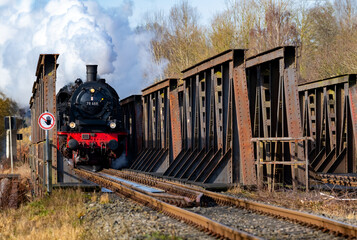 Steam train with historic locomotive and nostalgic coaches crossing steel rivet bridge in Ruhr...
