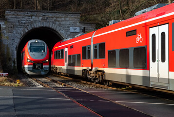 Two modern multiple unit trains meeting at “Schloßberg Tunnel“ and railroad crossing in Arnsberg Sauerland Germany. Public transport with diesel engines between Kassel and Hagen on Ruhr valley line - obrazy, fototapety, plakaty