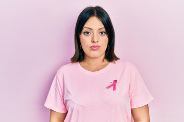 Fototapeta premium Young hispanic woman wearing pink cancer ribbon on t shirt relaxed with serious expression on face. simple and natural looking at the camera.