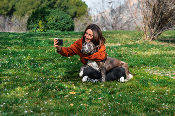 Una linda y alegre mujer caucásica está sentada en el parque, junto a su perro marrón de la raza...