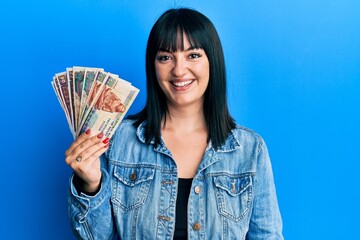 Young hispanic woman holding egyptian pounds banknotes looking positive and happy standing and smiling with a confident smile showing teeth - obrazy, fototapety, plakaty