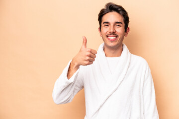 Young caucasian man wearing a bathrobe isolated on beige background smiling and raising thumb up