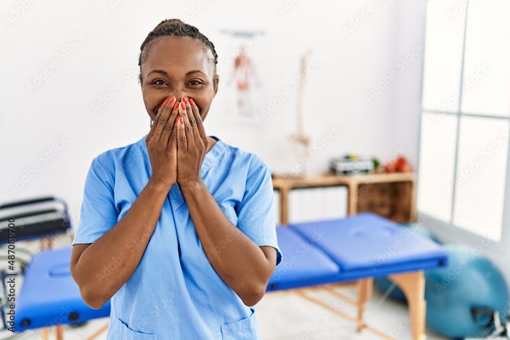 Wall mural black woman with braids working at pain recovery clinic laughing and embarrassed giggle covering mou