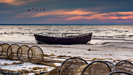 Coastal landscape at dawn with anchored old wooden fishing boat on sandy beach of the Baltic Sea