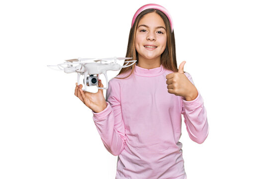 Beautiful brunette little girl using drone smiling happy and positive, thumb up doing excellent and approval sign