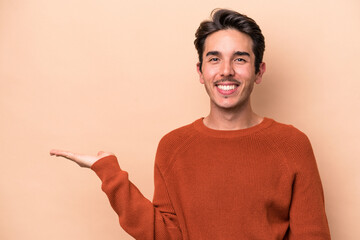 Young caucasian man isolated on beige background showing a copy space on a palm and holding another hand on waist.