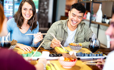 Multicultural gen z friends eating sushi with chopsticks at fusion restaurant winery - Food and beverage life style concept with happy people having fun together at eatery bar - Bright vivid filter