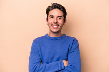 Young caucasian man isolated on beige background who feels confident, crossing arms with determination.