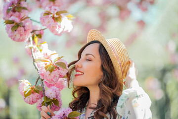 Happy young woman 30 years old in a wicker hat walks in a blooming city park. Portrait of a stylish...