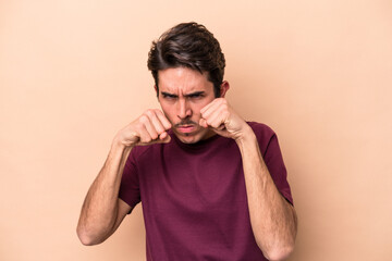 Young caucasian man isolated on beige background throwing a punch, anger, fighting due to an argument, boxing.