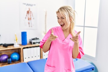 Young caucasian woman working at pain recovery clinic pointing fingers to camera with happy and funny face. good energy and vibes.