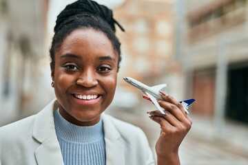 Young african american businesswoman smiling happy holding airplane toy at the city.