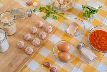 Kitchen table with meatballs ready for pan, wooden cutting board and raw ingredients