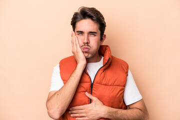 Young caucasian man isolated on beige background blows cheeks, has tired expression. Facial...