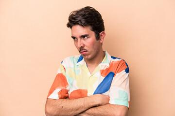 Young caucasian man isolated on beige background tired of a repetitive task.