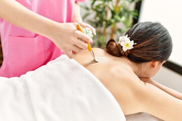 Middle age hispanic woman having aloe vera cream back massage at beauty center