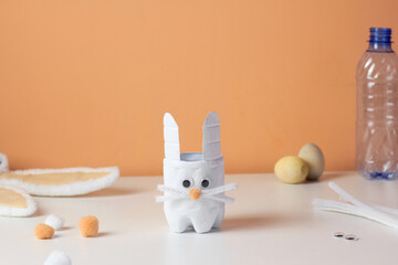 Easter bunny craft from plastic bottle. Kids DIY home activities. Handmade cute toy rabbit on table. Reuse concept