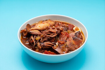 fresh tasty squid stew in white bowl on blue
