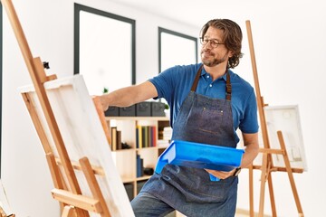 Middle age caucasian man smiling confident drawing using paint roller at art studio