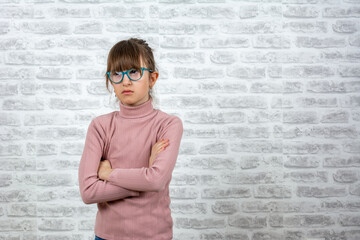 Angry school girl over white brick wall background, sign and gesture concept. Little girl with...