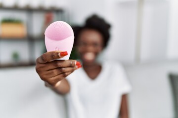 Young african american woman smiling confident using electric facial cleaner at home