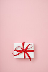 Gift box wrapped in white paper and decorated with red ribbon laid out on a flat surface