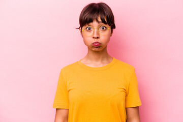Young hispanic woman isolated on pink background blows cheeks, has tired expression. Facial expression concept.
