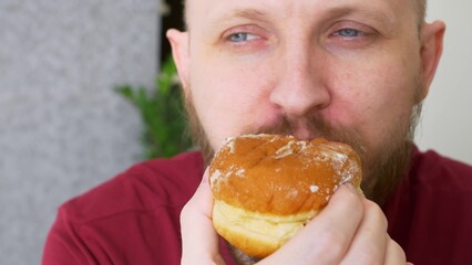 Close-up of a man biting a delicious donut and admiring its taste, powdered sugar remains on his mustache. Eating high calorie foods. Delicious pastry is the favorite food of the cops