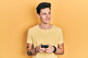 Young hispanic man using smartphone typing message smiling looking to the side and staring away thinking.