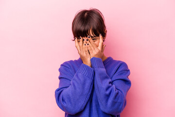 Young hispanic woman isolated on pink background blink at the camera through fingers, embarrassed covering face.