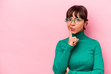 Young hispanic woman isolated on pink background looking sideways with doubtful and skeptical expression.