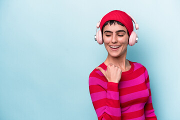 Young caucasian woman listening to music isolated on background points with thumb finger away, laughing and carefree.