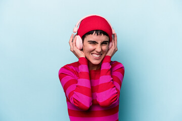 Young caucasian woman listening to music isolated on background covering ears with hands.