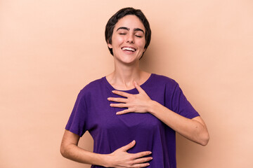 Young caucasian woman isolated on beige background laughs happily and has fun keeping hands on...