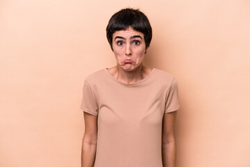 Young caucasian woman isolated on beige background shrugs shoulders and open eyes confused.