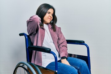 Young brunette woman sitting on wheelchair suffering of neck ache injury, touching neck with hand,...