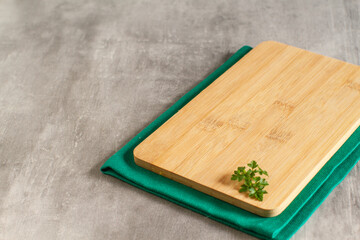 Empty wooden  kitchen board and green towel on a grey background 